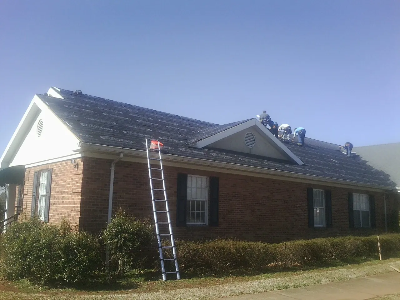 Crew tearing shingles off a brick ranch roof with a ladder set — Metal Roof Repair work by our crew in Montrose